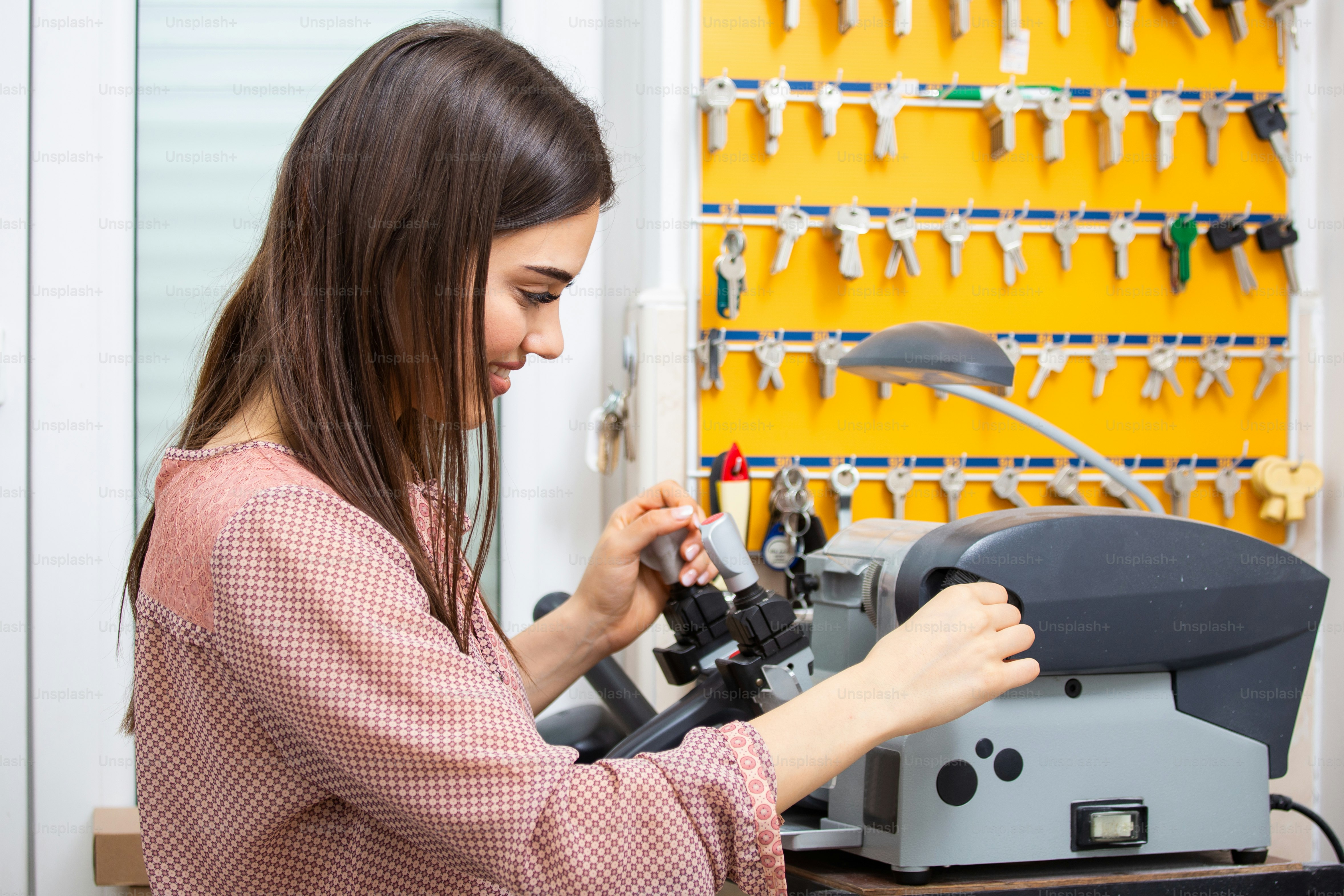 Professional skilled key cutter making door keys copies in locksmith. Young professional with different types of keys in locksmith